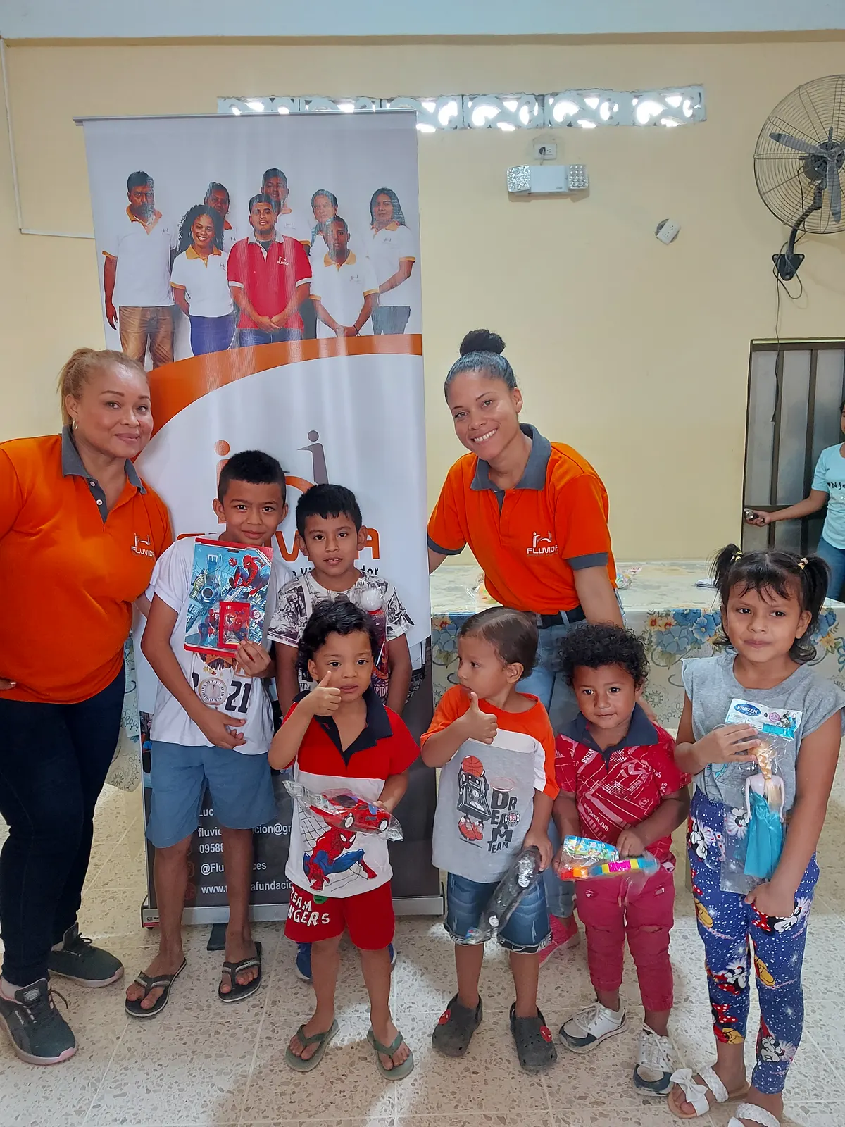 Voluntarias de Fluvida con niños y niñas que recibieron juguetes, frente al banner de la fundación